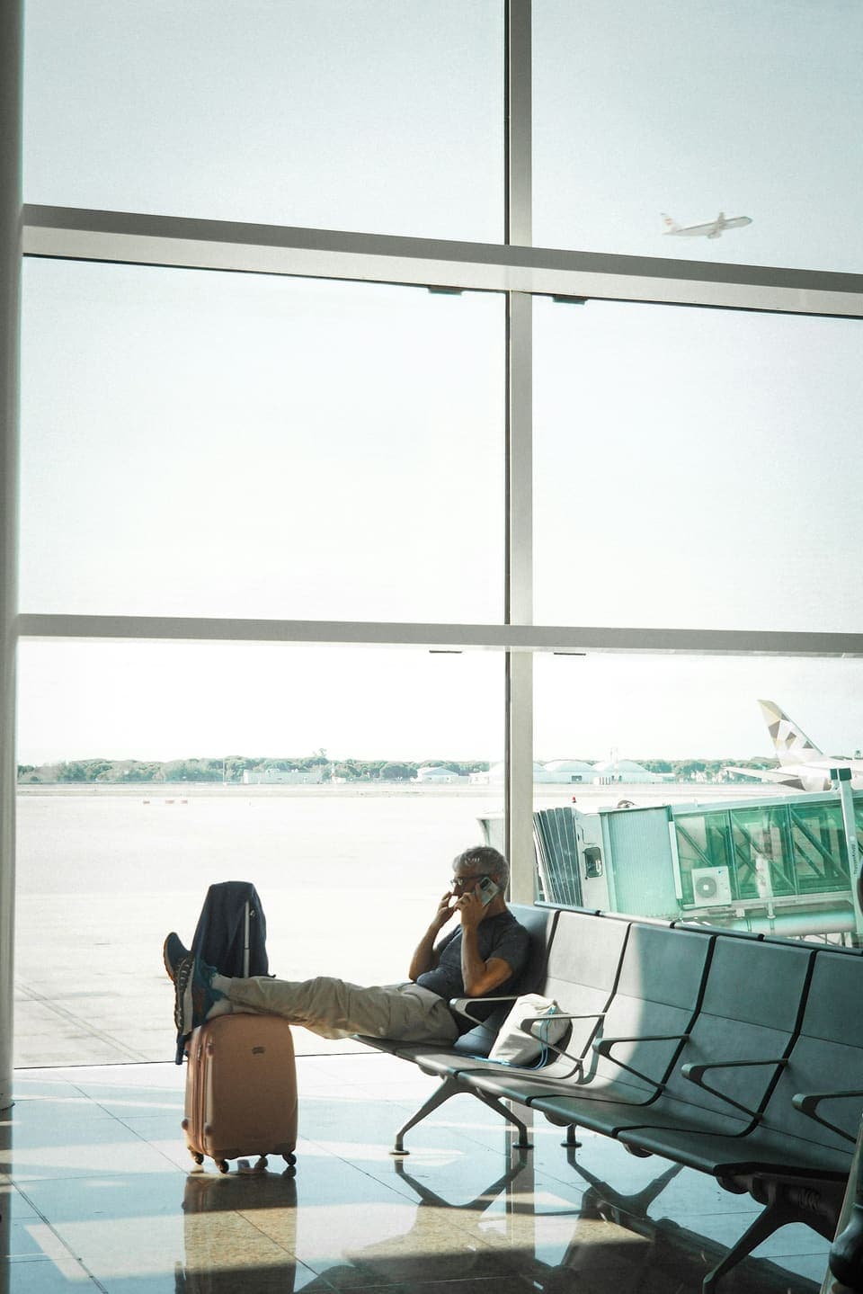 A business traveller on the phone at an airport gate with a suitcase