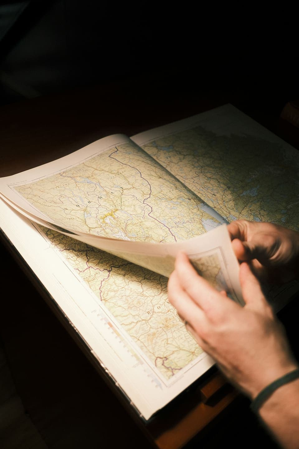 Hands turning the pages of a detailed road atlas