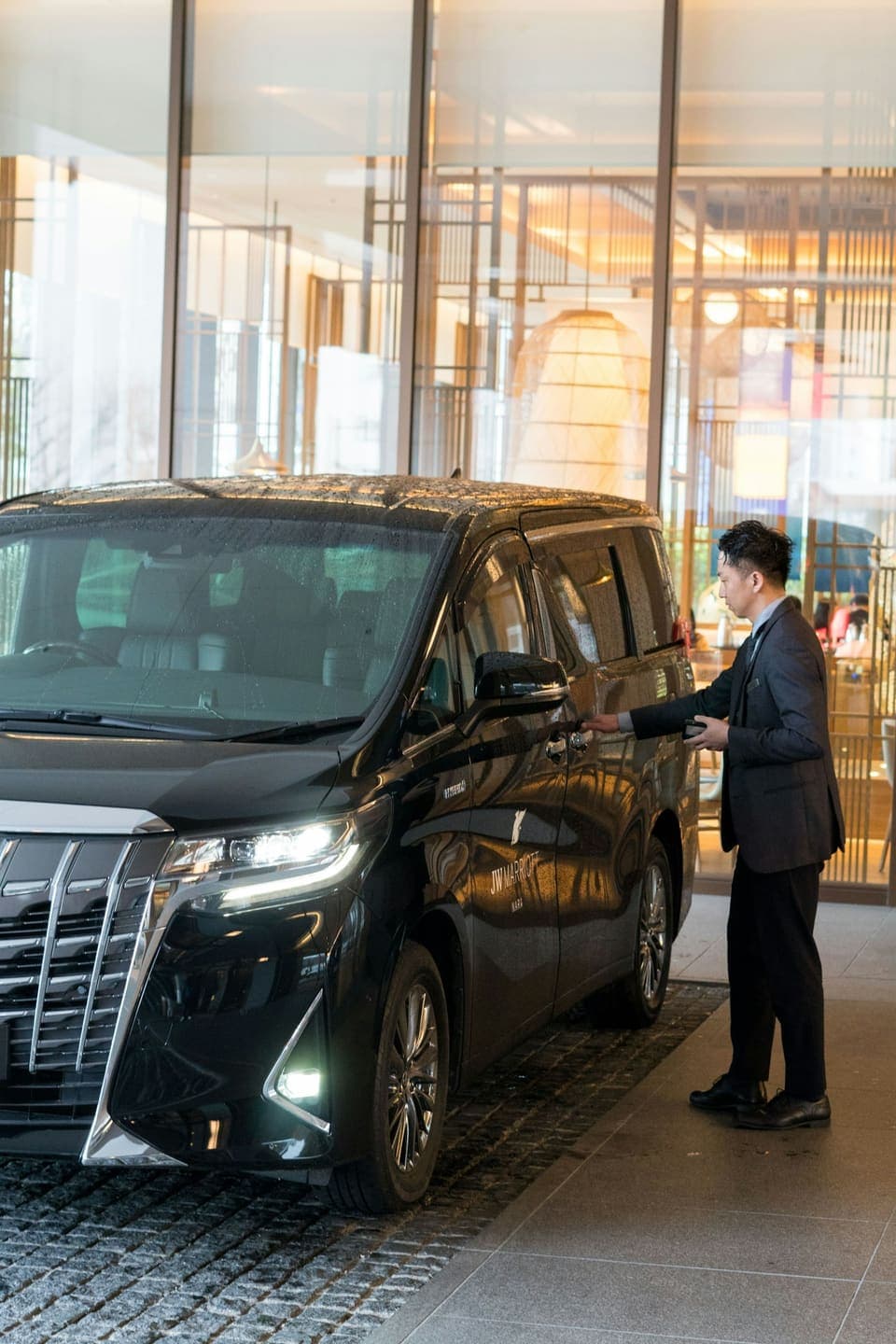 A driver in a suit opening the door of a van for arriving guests