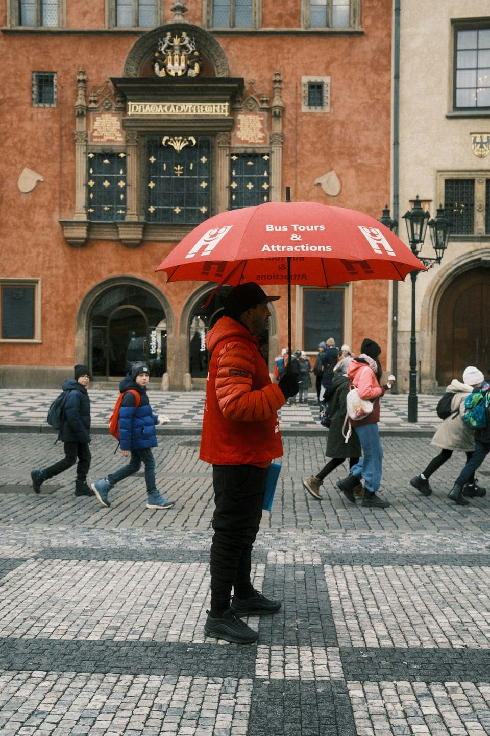 A tour guide with a red umbrella leading a group through an old town square